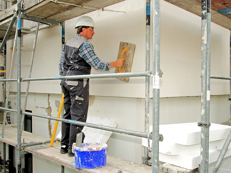 Handwerker glättet Wärmedämmung mit Glättbrett an Hauswand – Facharbeit eines Stuckateurs in Iserlohn.