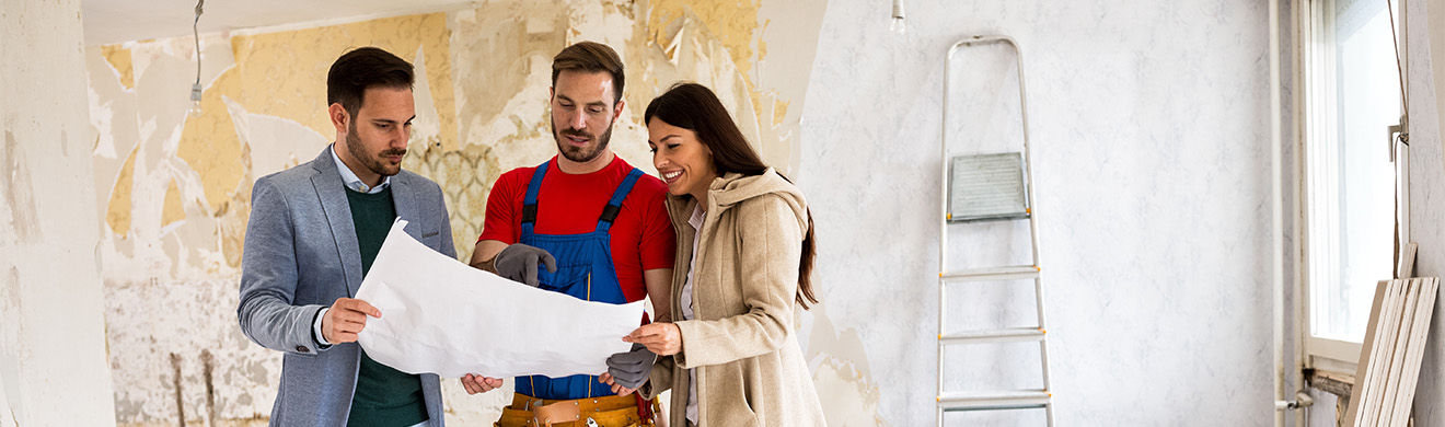 Junges Paar betrachten Baupläne für ihre Hausrenovierung gemeinsam mit einem Handwerker in ihrem Zuhause.