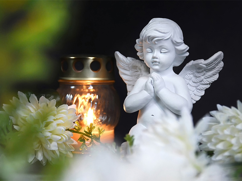 Brennende Kerze im Glas, Engelsfigur und Blume – Ausdruck von Mitgefühl und Erinnerung bei Feuerbestattung Iserlohn.