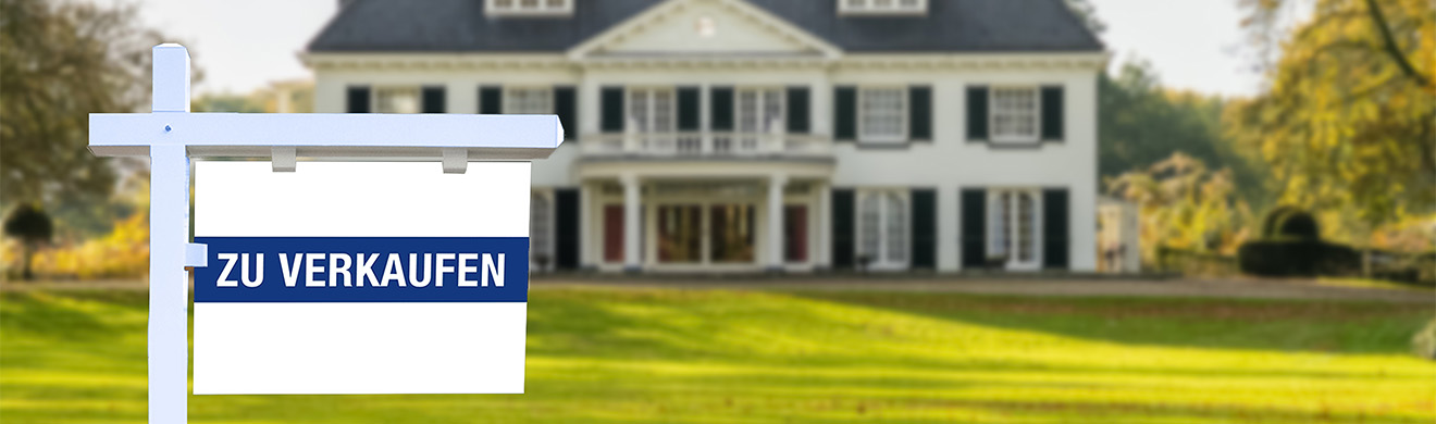 Hausverkaufsschild vor modernem Haus im Grünen, das einen anstehenden Immobilienverkauf in Iserlohn symbolisiert.