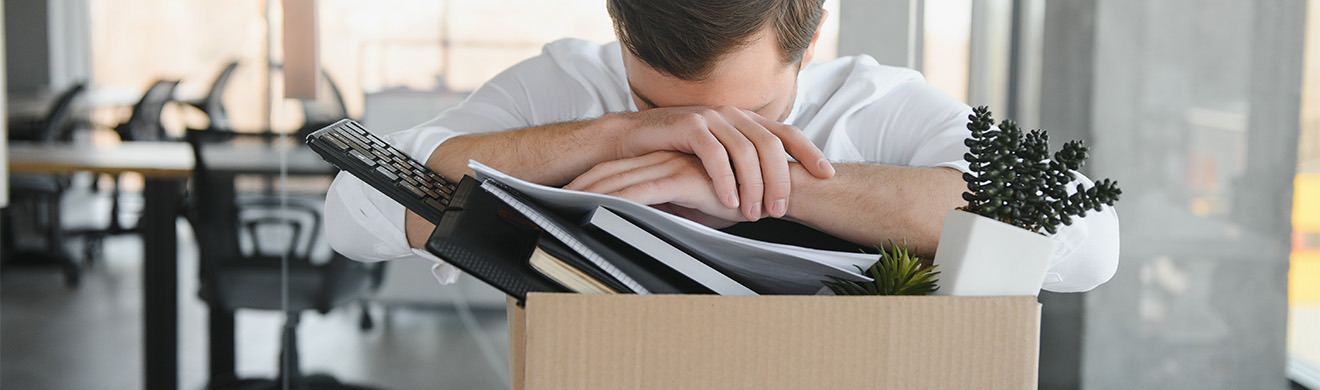 Enttäuschter Büroangestellter trägt Karton mit persönlichen Sachen nach Jobverlust, symbolisiert Kündigungsschutzklage in Iserlohn.