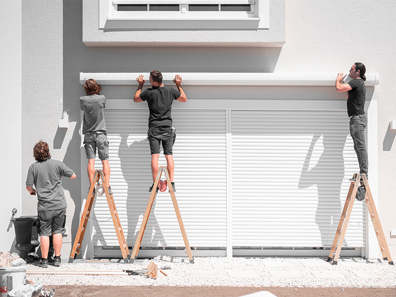 Vier Handwerker hängen eine Markise an Halterungen an einer Hauswand an, teamwork Montage für sicheren Sonnenschutz, sonniger Tag.